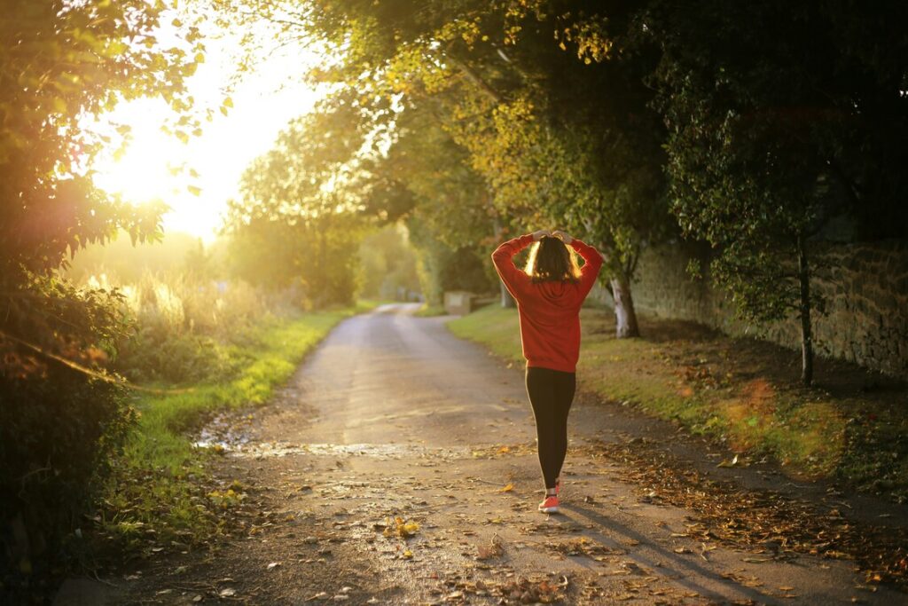 saúde-mental-importa Imagem de pessoa pensativa caminhando em um parque ao pôr-do-sol com as mãos sobre a cabeça