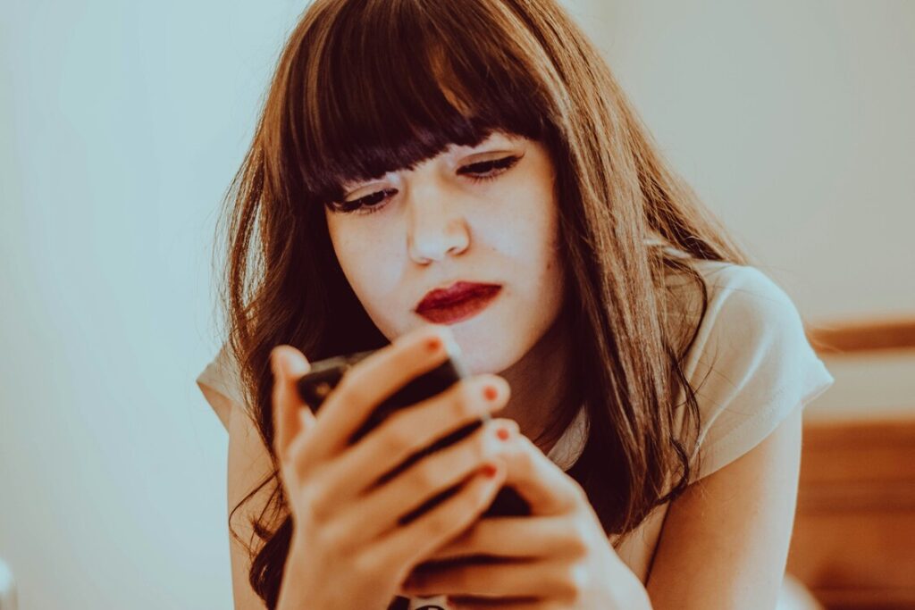 ansiedade-rede-social Imagem de mulher com o celular na mão e semblante pensativo