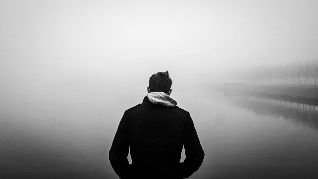 Imagem preta e branca de homem de frente para um lago pensativo representando alguém que está em depressão